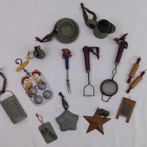 May include: A collection of miniature kitchen-themed ornaments in various shapes and colors. Includes a grater, rolling pins, a star, a muffin tin with snowmen, and a miniature washboard. Each ornament has a loop for hanging.