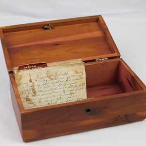 May include: Open wooden recipe box with a hinged lid, revealing recipe cards inside. The box is made of reddish-brown wood and has a brass latch. The recipe cards are handwritten and show signs of age.