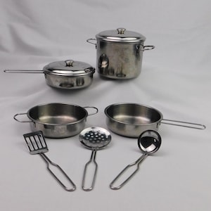 May include: A set of miniature stainless steel cookware, including a pot with a lid, a saucepan, two frying pans, a spatula, a slotted spoon, and a ladle. The set is designed for play or display.