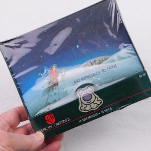 May include: A boxed set of American Greetings self-mailers. The box features a winter scene with a figure on skis and the text "...AND ESPECIALLY TO YOU!". The box also has a cartoon dog sticker and the text "12 SELF-MAILERS 12 SEALS".