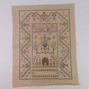 May include: A vintage cross-stitch sampler on tan fabric. The design features an alphabet, floral arrangements, a house, and figures. The border is a green chain stitch with floral and butterfly motifs. The color palette includes pink, yellow, and green.