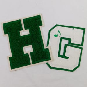 May include: Two varsity letter patches, one green "H" and one white "G" with a green border. The "G" features a green musical note. These patches are likely for a school or team.