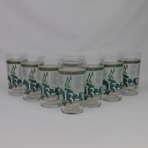 May include: Set of nine clear drinking glasses. Each glass features a green and white design with the text "132 Kentucky Derby" and a horse graphic. The glasses are cylindrical and appear to be made of glass.