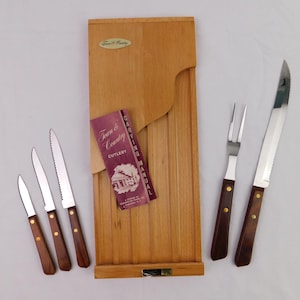 May include: A wooden carving board with a set of knives, a carving fork, and a carving knife. The knives have serrated blades and wooden handles. A booklet titled "Town & Country Cutlery" is also included.