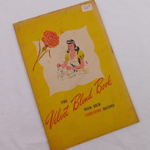 May include: A vintage yellow recipe booklet titled The Velvet Blend Book Milk-Rich Carnation Recipes. The cover features an illustration of a person in a polka-dot apron mixing ingredients, an orange carnation flower, and a small price tag of 25 cents.