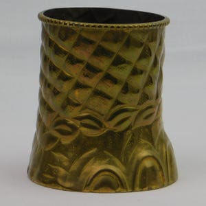 May include: A decorative brass-colored vase with a textured diamond pattern on the upper portion and leaf-like designs on the lower portion. The vase has a dark interior and a detailed rim.