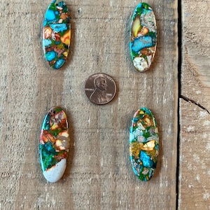 May include: Four oval-shaped, colorful, and patterned stones with a copper-like finish. The stones are arranged in a row on a wooden surface.
