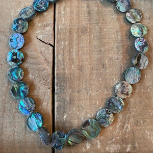May include: A strand of round, iridescent abalone shell beads in shades of green, blue, and brown. The beads are strung on a clear thread and are arranged in a circle.