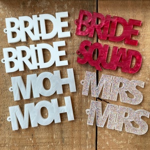 May include: Six acrylic signs with different text. Two white signs say "BRIDE" and two white signs say "MOH". One red sign says "BRIDE SQUAD" and one glittery sign says "MRS".