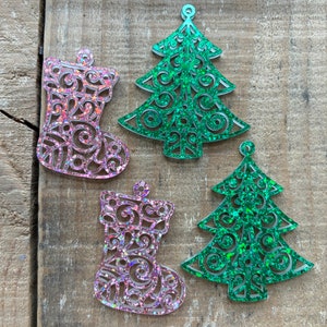 Puede incluir: Cuatro adornos navideños, dos árboles verdes y dos calcetines rosas, todos con un acabado brillante y un diseño de encaje.