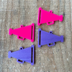 May include: Four plastic megaphone charms in pink and purple. The megaphones are approximately 2 inches long and have a hole at the top for hanging.