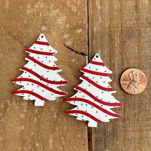 May include: Two white Christmas tree ornaments with red and green candy cane stripes. The ornaments are on a wooden background.