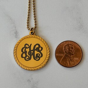 May include: Gold necklace with a round pendant featuring a monogram of the letters "EHS" in a decorative script font. The pendant has a rope-like border. The necklace is shown next to a US penny for scale.