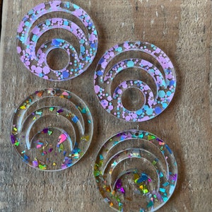 May include: Four clear acrylic circles with a layered crescent moon design. Each circle is filled with iridescent glitter in various colors, including pink, blue, and purple.