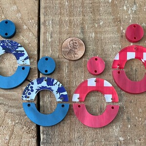 May include: Two sets of unfinished wooden earrings. One set is red with a white checkered pattern and the other is blue with a white floral pattern.