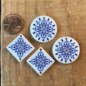 May include: Four white ceramic tiles with blue and black floral designs. Two tiles are round and two are square.