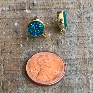 May include: A pair of gold-tone earring posts with a round, blue and green glitter-covered charm. The charms are about the size of a US penny.