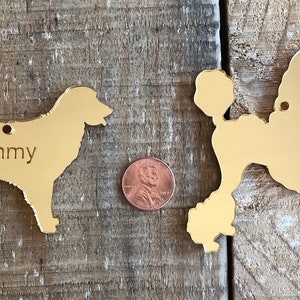 May include: Two gold-colored metal dog silhouette ornaments. The ornament on the left is a golden retriever with the name "Sammy" engraved on it. The ornament on the right is a poodle.