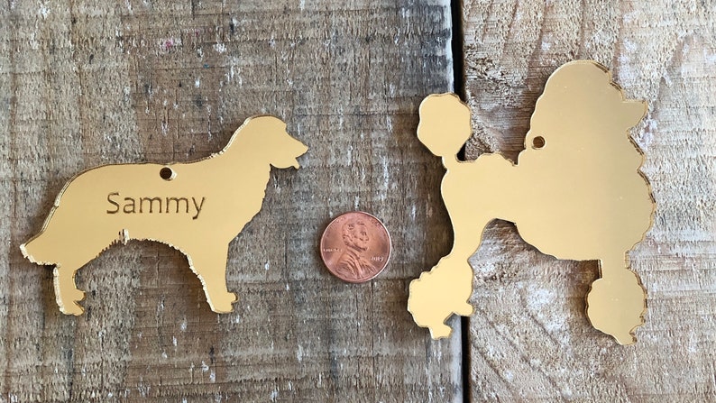 May include: Two gold-colored metal dog silhouette ornaments. The ornament on the left is a golden retriever with the name "Sammy" engraved on it. The ornament on the right is a poodle.
