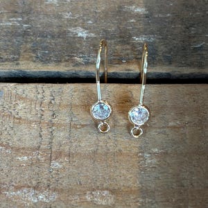 May include: A pair of gold-toned earring hooks with clear round stones.