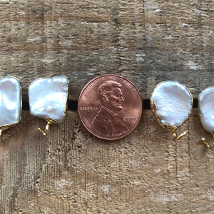 May include: A pair of white baroque pearl earrings with gold hooks. The pearls are approximately the size of a US penny.