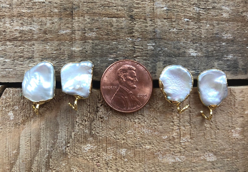 May include: A pair of white baroque pearl earrings with gold hooks. The pearls are approximately the size of a US penny.