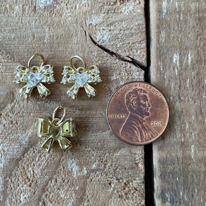 May include: Three gold-tone bow charms with clear rhinestones. The charms are about the size of a US penny.