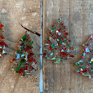 May include: Four clear plastic Christmas tree ornaments with red and green glitter. The ornaments are on a wooden surface.