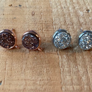 May include: Two pairs of round, sparkly earrings. One pair is rose gold with brown glitter, and the other pair is silver with white glitter.