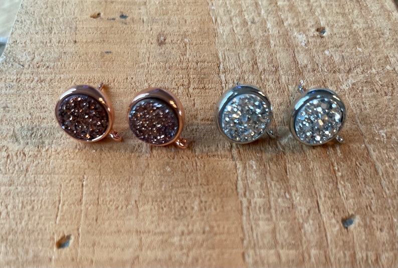 May include: Two pairs of round, sparkly earrings. One pair is rose gold with brown glitter, and the other pair is silver with white glitter.