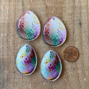 May include: Four plastic Easter egg-shaped ornaments with floral designs. Two ornaments have a green, pink, and yellow floral design. The other two ornaments have a blue, pink, and yellow floral design.