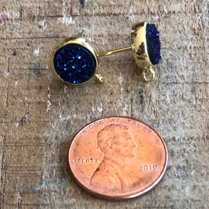 May include: A pair of gold stud earrings with blue glitter round cabochons. The earrings are about the size of a US penny.