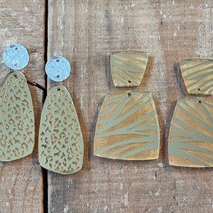 May include: Two pairs of gold-tone earrings with different patterns. One pair features a leopard print and the other pair features a zebra print.