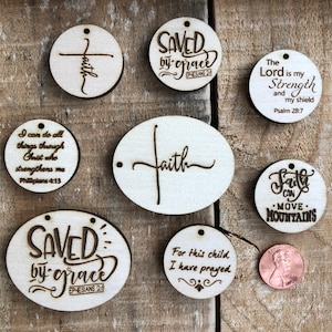 May include: Eight wooden ornaments with inspirational Christian quotes and verses. The ornaments are round and oval shaped with a hole at the top for hanging. The quotes include "Saved by Grace", "Faith", "The Lord is my Strength and my Shield", and "Faith can move mountains".