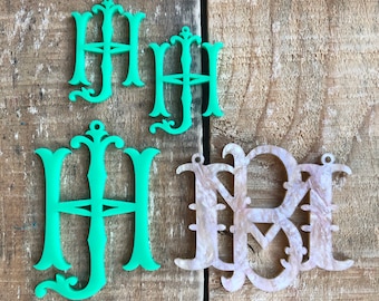 May include: Three decorative monograms, two in a light green color and one in a light pink color. The monograms are all in the same style, with a decorative flourish at the top and bottom. The monograms are all the letter "H".