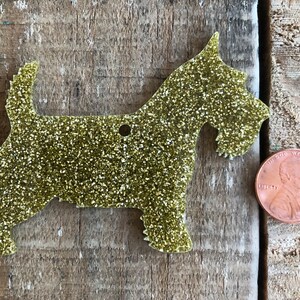 May include: Gold glitter Scottie dog ornament. The ornament is about the size of a US penny.