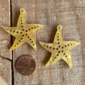 May include: Two yellow plastic starfish with a hole at the top for hanging. The starfish have a dotted pattern and are about the size of a US penny.
