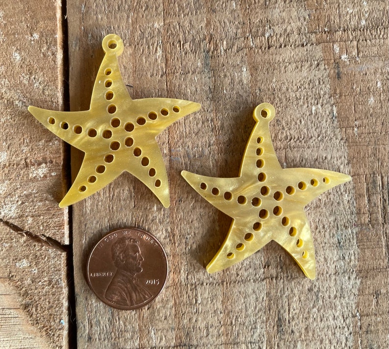 May include: Two yellow plastic starfish with a hole at the top for hanging. The starfish have a dotted pattern and are about the size of a US penny.