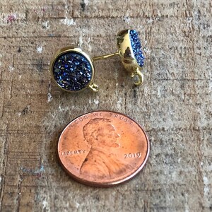 May include: A pair of gold-toned earrings with blue glitter-like stones. The earrings are round and have a small loop on the back for attaching to an earring hook.
