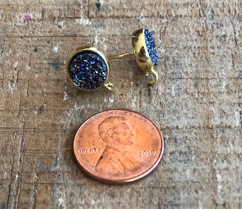May include: A pair of gold-toned earrings with blue glitter-like stones. The earrings are round and have a small loop on the back for attaching to an earring hook.