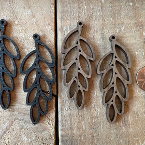 May include: Three black wooden leaf-shaped earrings with a hole at the top for hanging. The earrings are about the size of a US penny.