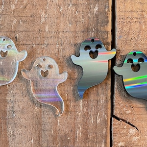 May include: Four iridescent ghost-shaped ornaments with a smiling face cutout. The ghosts are made of clear acrylic with a rainbow iridescent finish.