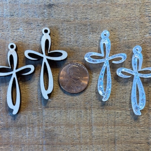 May include: Four decorative cross pendants in varying sizes. Two are made of light wood, and two are clear with glitter. A penny is included for size comparison. The crosses have a looped top for hanging.