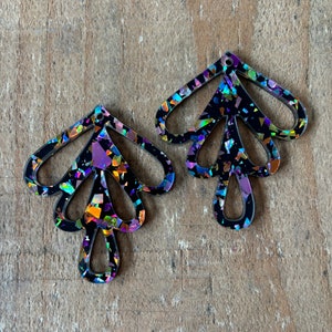 以下が含まれることがあります： 虹色のグリッター仕上げの黒いイヤリングのペア。イヤリングは、複数の枝を持つスタイリッシュな木の形をしています。