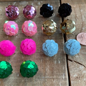 May include: Assortment of 10 pairs of round, sparkly, colorful earrings. The earrings are made of sequins and are available in pink, blue, green, gold, and black.