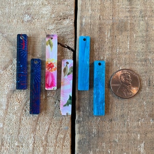 May include: Six different rectangular acrylic charms with various patterns. The charms are blue, pink, and white with floral and geometric designs.