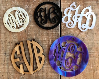 May include: Five different round wooden and acrylic ornaments with cut-out monogram letters. The ornaments are in white, black, brown, purple, and white.