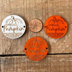 May include: Three wooden round ornaments with the text "Hello Pumpkin" in a cursive font. The ornaments are decorated with a pumpkin and a leopard print pattern. One ornament is white, and the other two are orange.