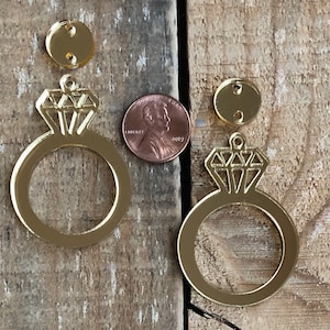 May include: Two gold mirror acrylic ring and diamond charms. The charms are approximately the size of a US penny.