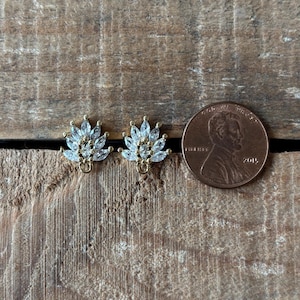 Puede incluir: Dos postes de pendientes de tono dorado con un grupo de piedras claras en forma de marquesa. Los pendientes son aproximadamente del tamaño de una moneda de un centavo de dólar estadounidense.